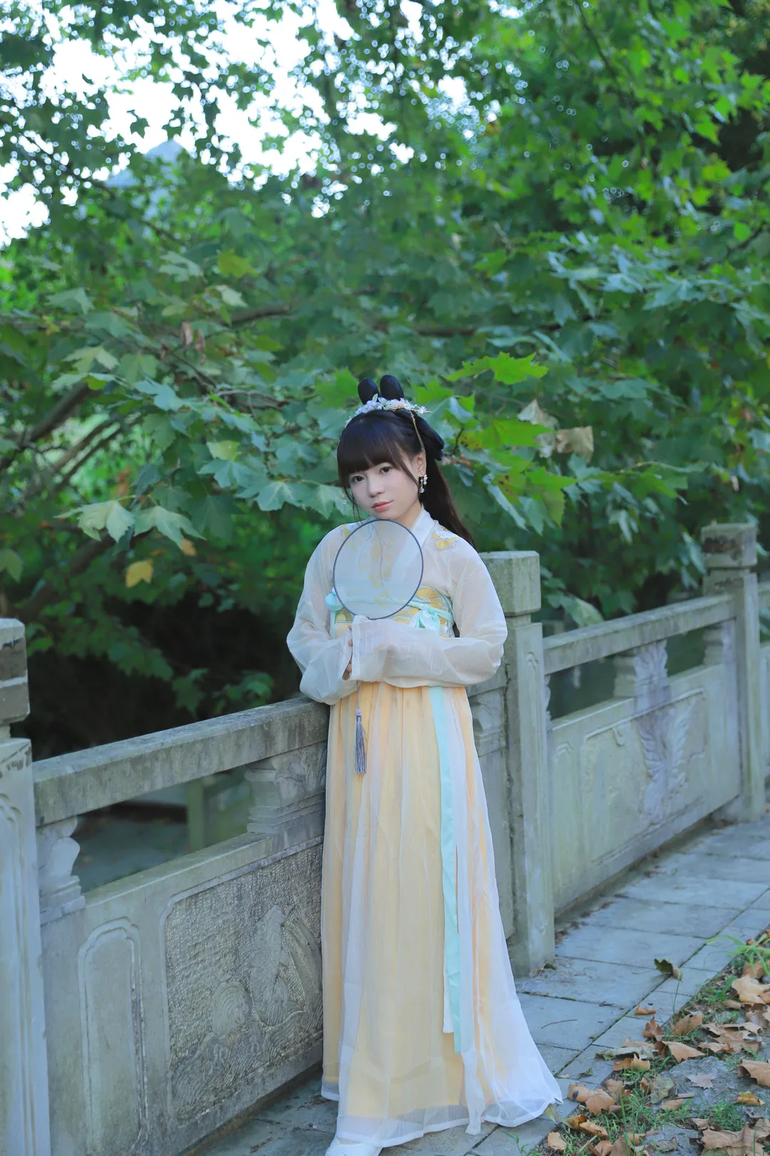 晓晓可可爱身着鹅黄配浅蓝汉服手持团扇站在石桥护栏旁的全身照