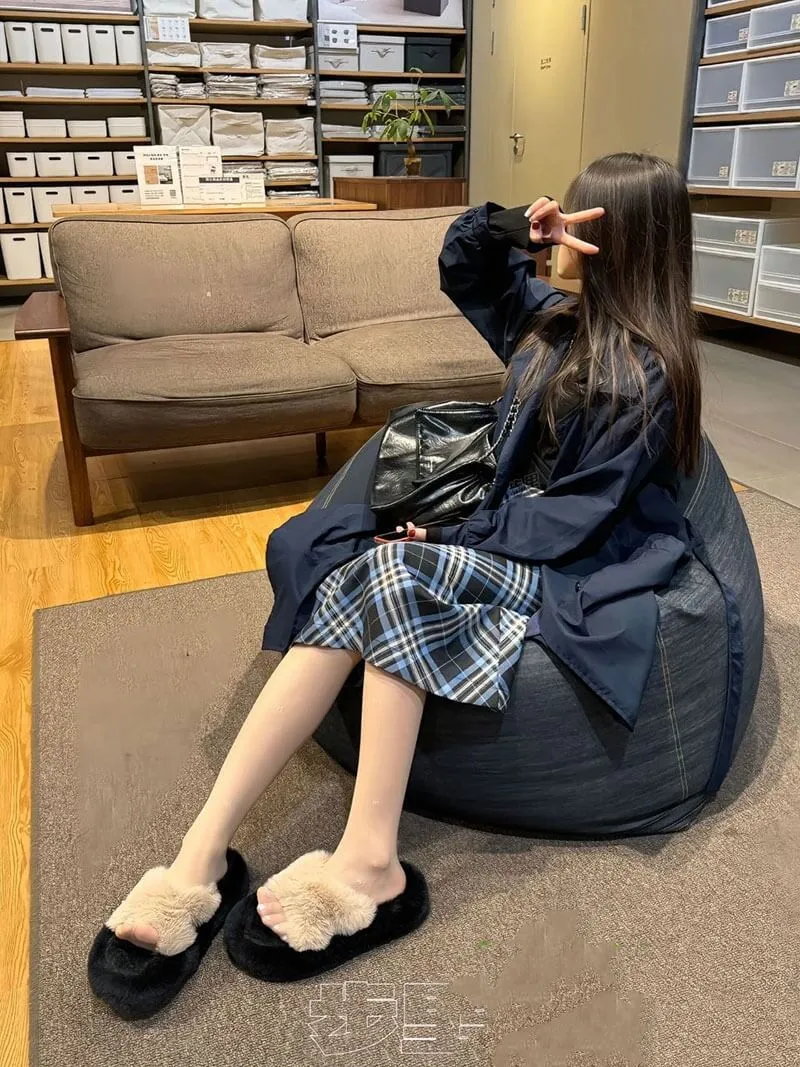 室内原木色家具展厅内，模特倚坐于深灰色豆袋沙发，身穿深蓝色外套与蓝黑格纹半身裙