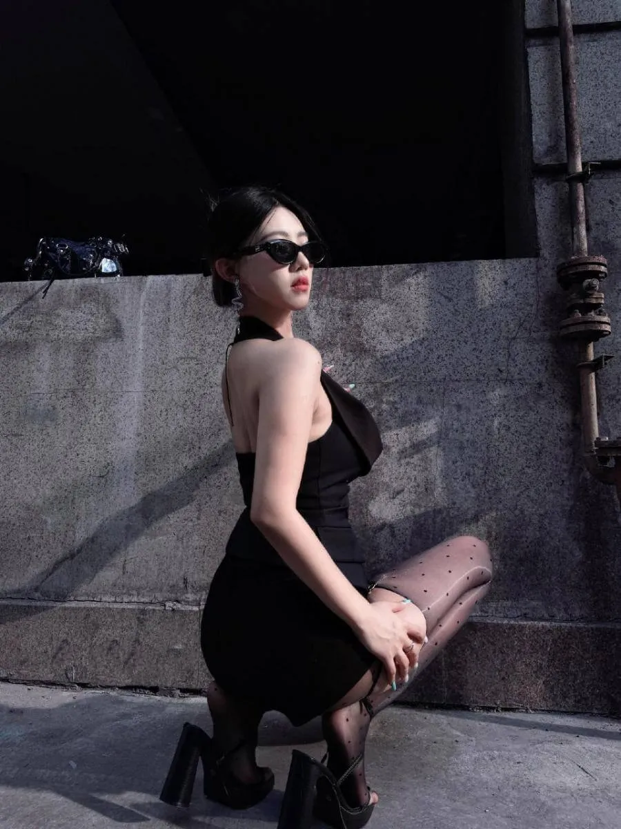 抖音小野马佩戴墨镜身穿黑色挂脖露背短裙单膝跪地的户外侧身全身照