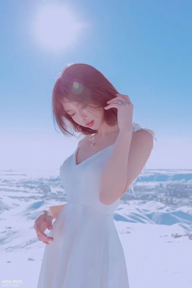 晴空雪山背景下身穿白色吊带无袖连衣裙迎着高光抬手的短发女性半身照